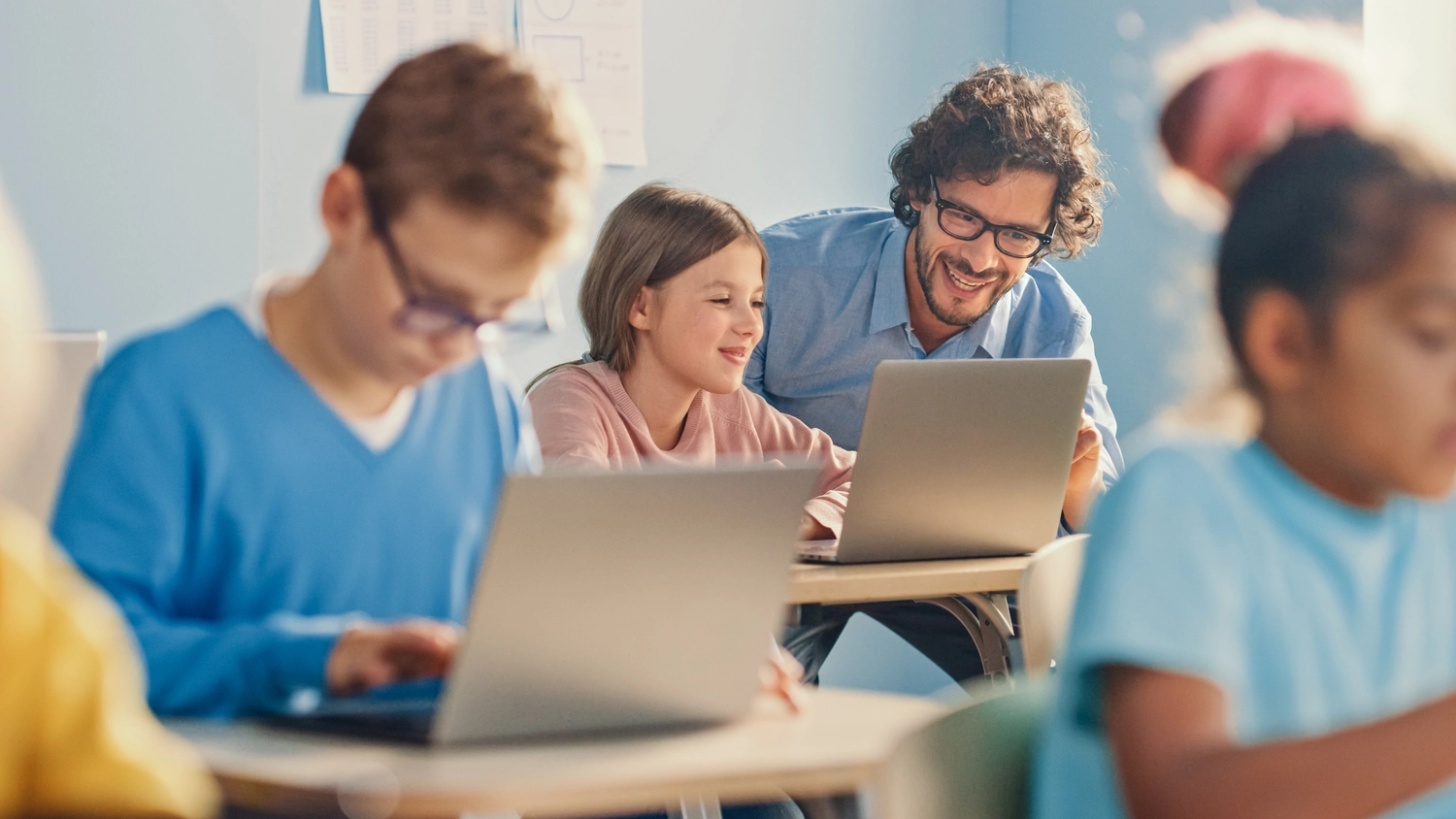 Informatikunterricht in der Grundschule: Kluges Mädchen benutzt Laptop, freundliche Lehrerin hilft ihr, indem sie ihr den Unterricht und die Aufgabe erklärt.